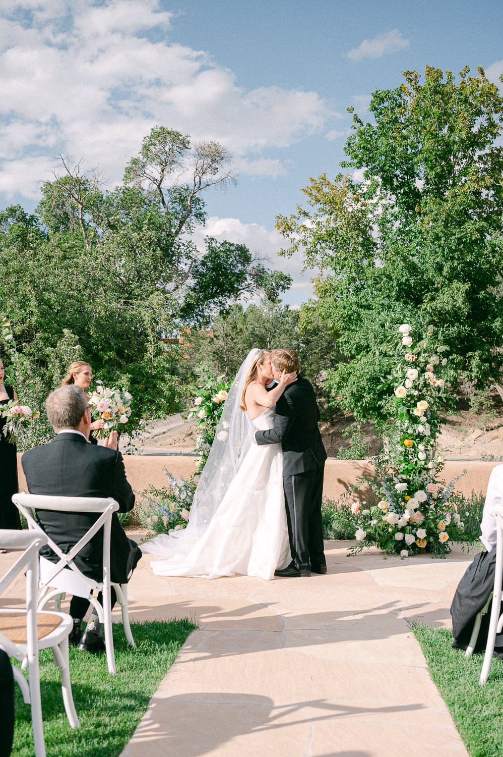 Bride and Groom kiss in front of a flower altar during an outdoor wedding ceremony.