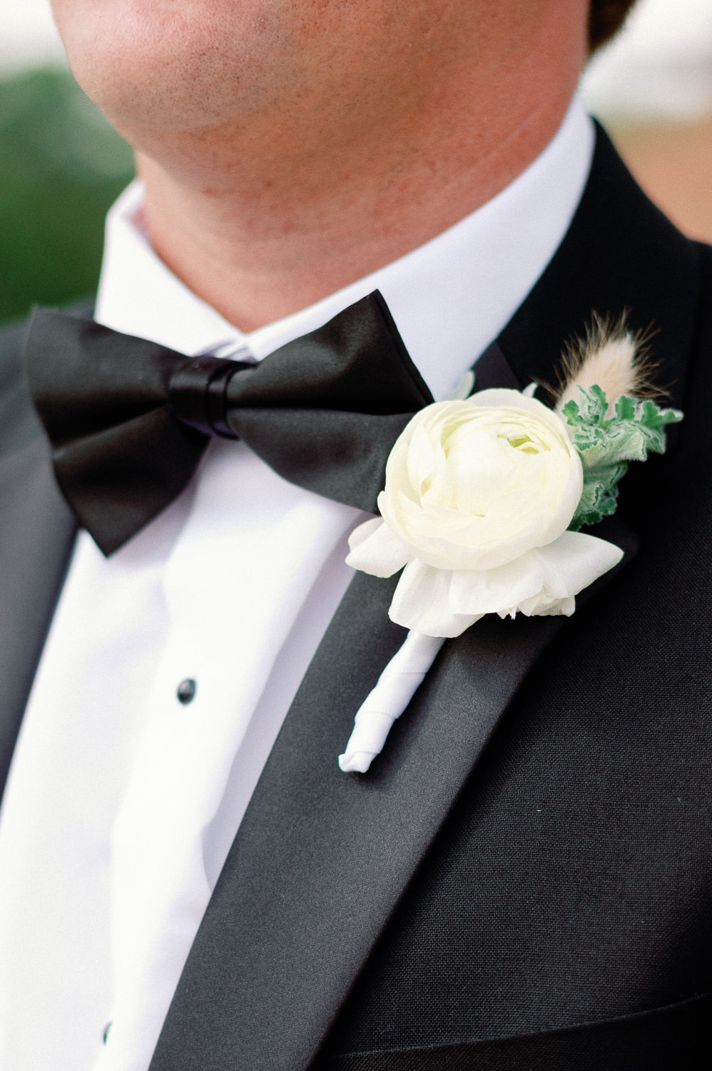 Close up of a white ranunculus boutonnière on a groom in a black tux.