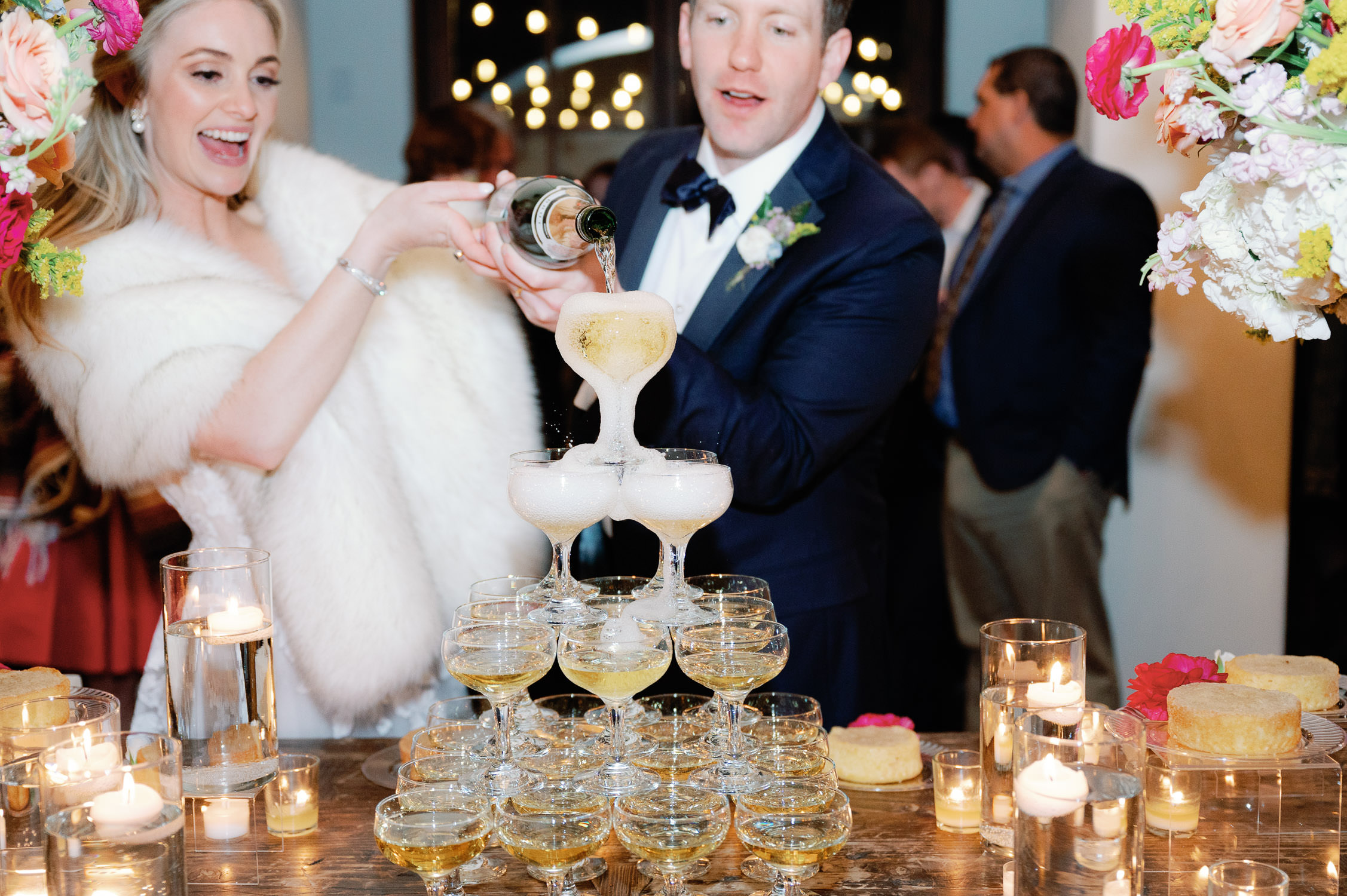 Bride and Groom smile as they pour champagne into the top glass of a champagne tower