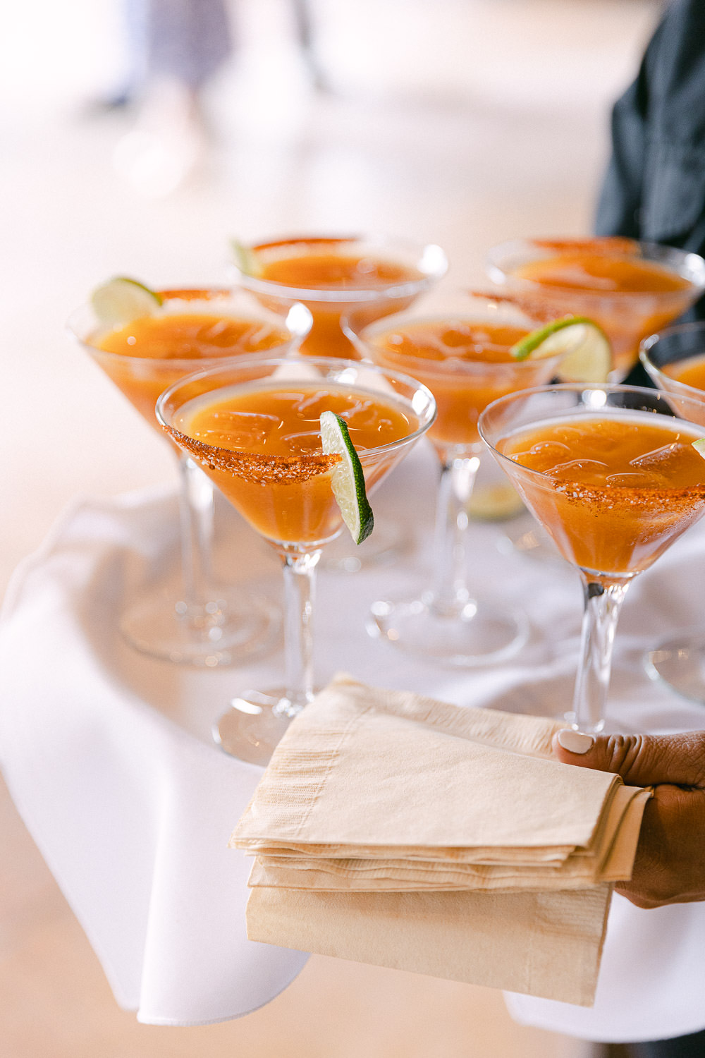 Close up of a tray of orange colored martinis with lime and spices on the rim.