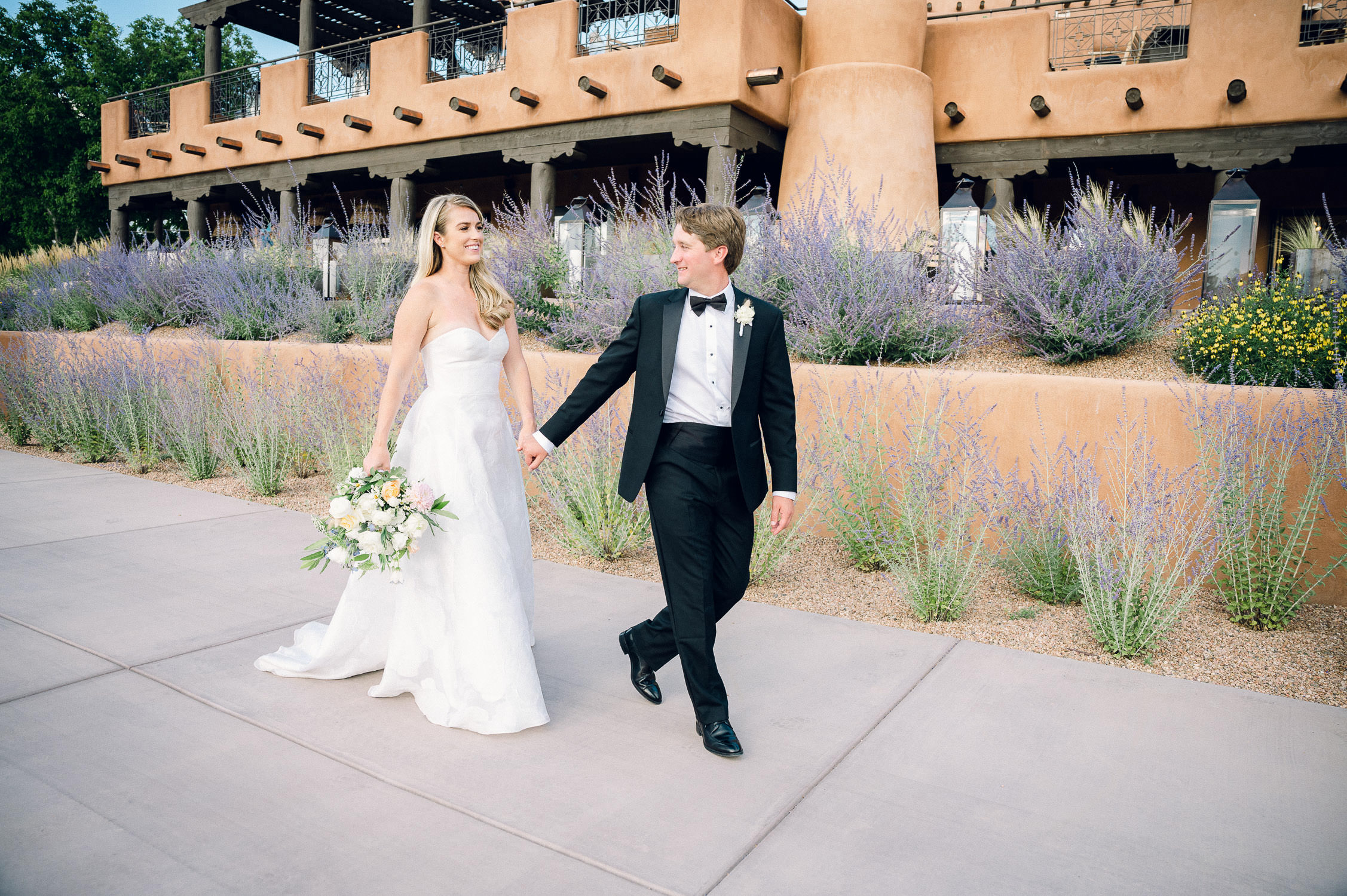 Bride and groom walk hand in hand in front of Bishop's Lodge in Santa Fe.