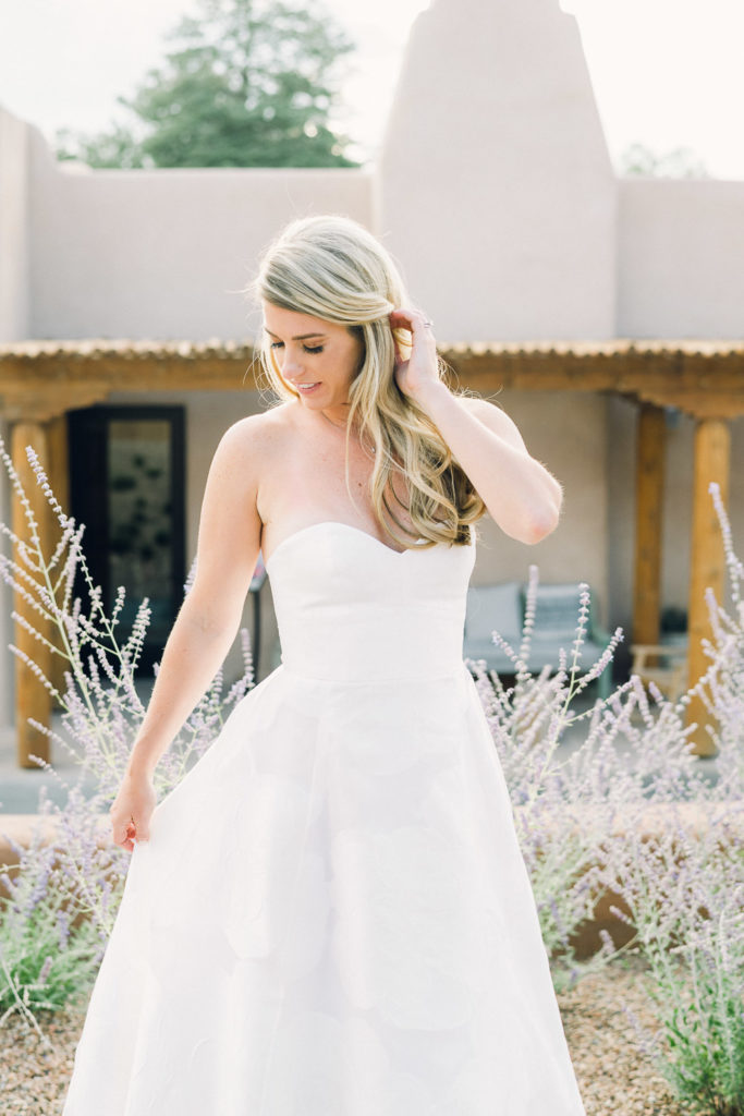Bride pulls her hair back in front of an adobe building.