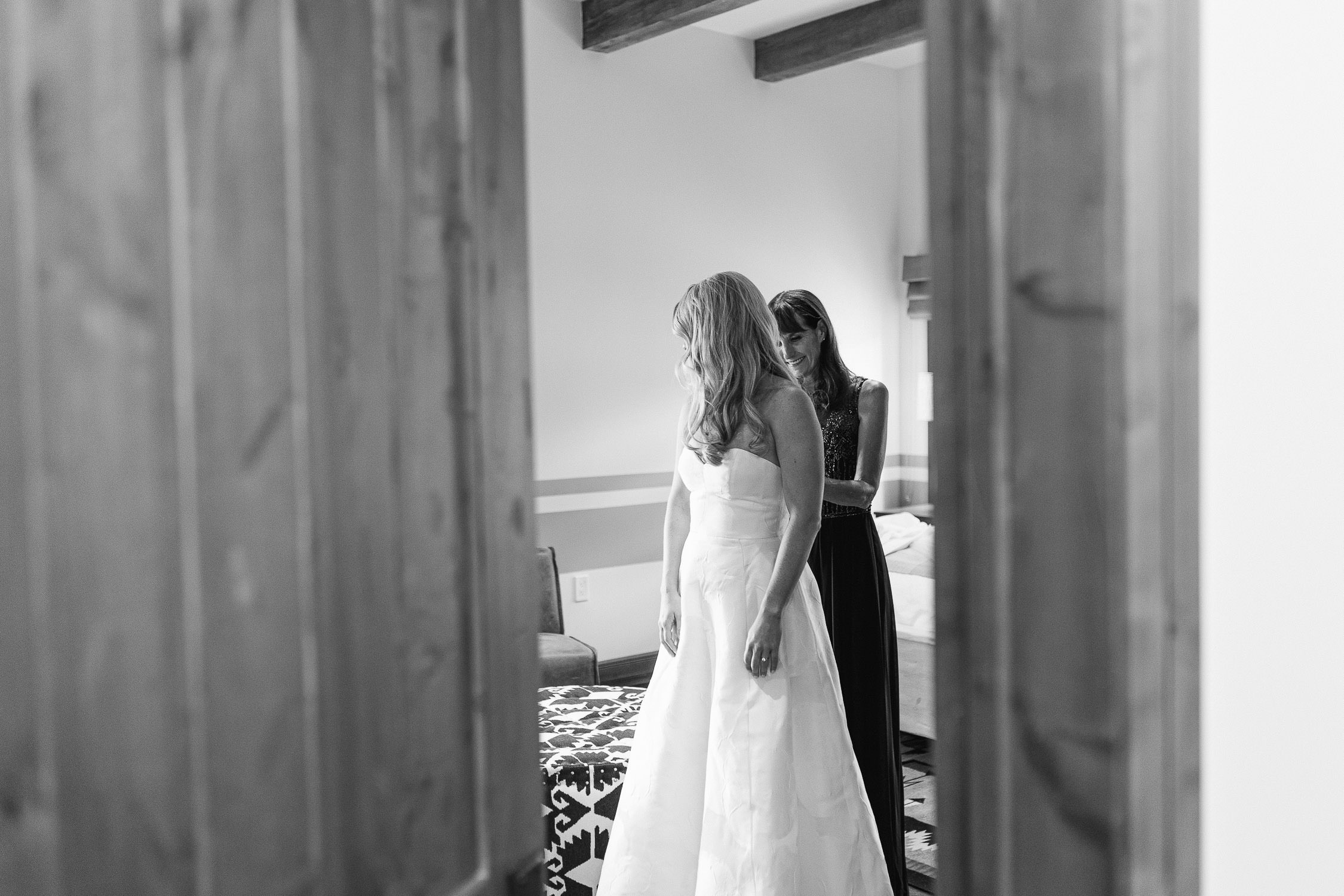 Black and white images of mother zipping up her daughter's dress on her wedding day.