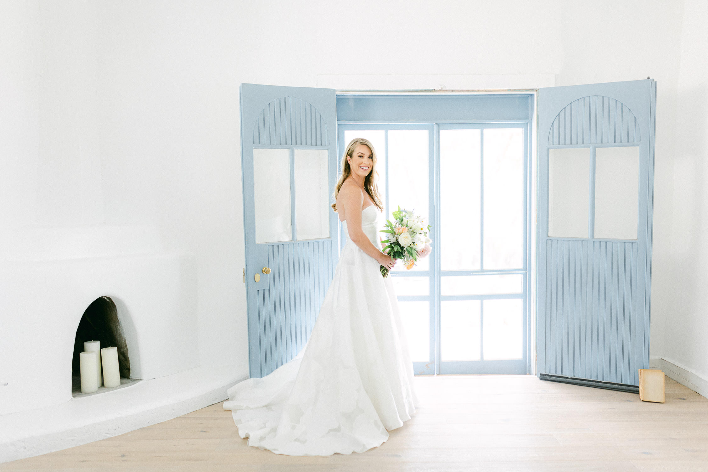 Bride in a classic strapless dress holds bouquet in front of blue doors.
