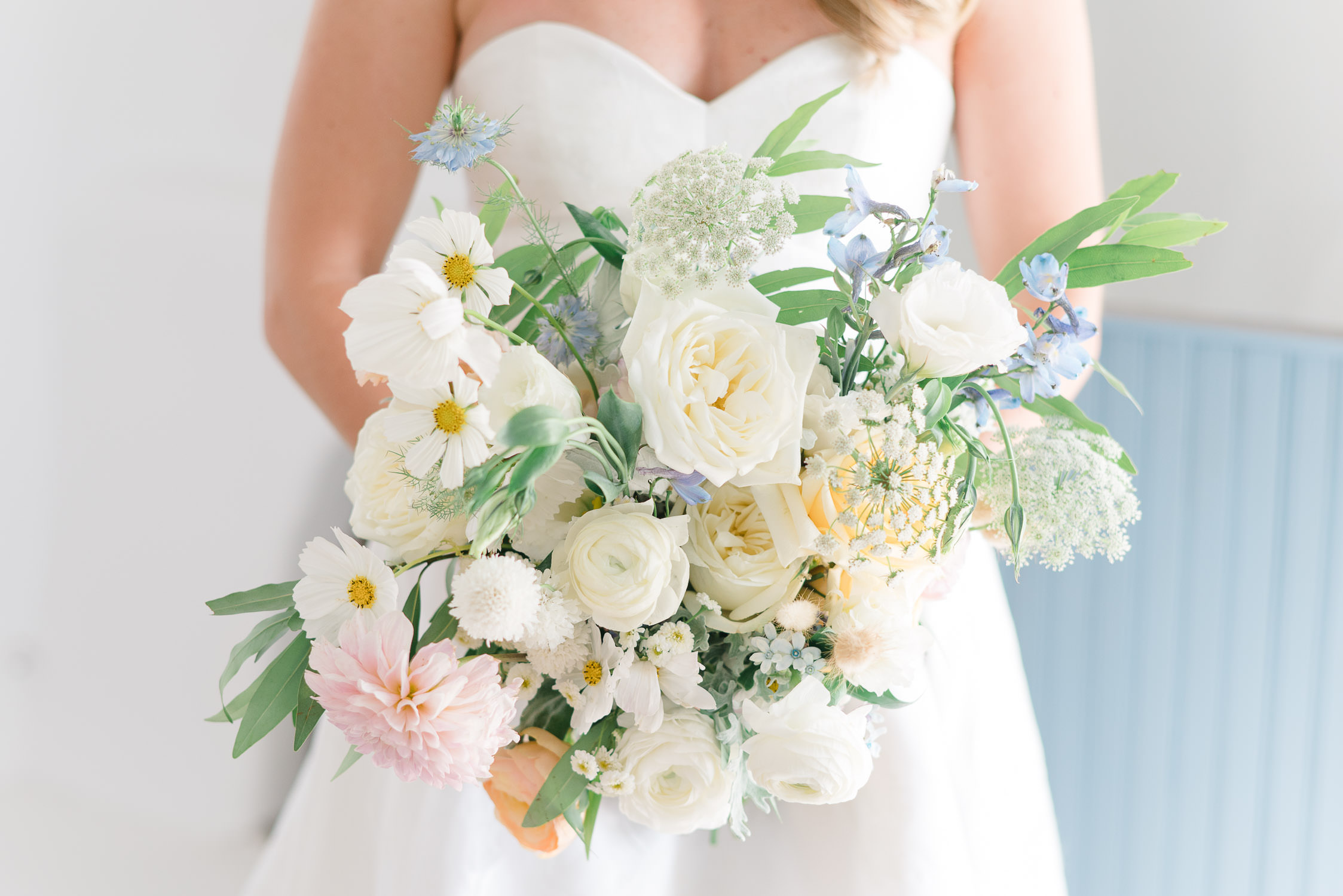 Close up of bride holding wedding bouquet with blue, pink and white flowers.