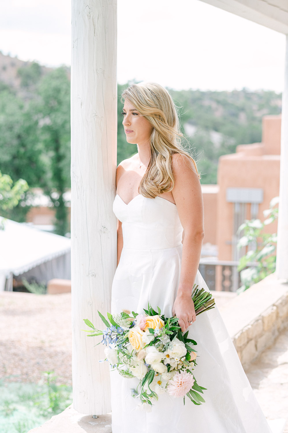 Bride leans against a column holding a bouquet.