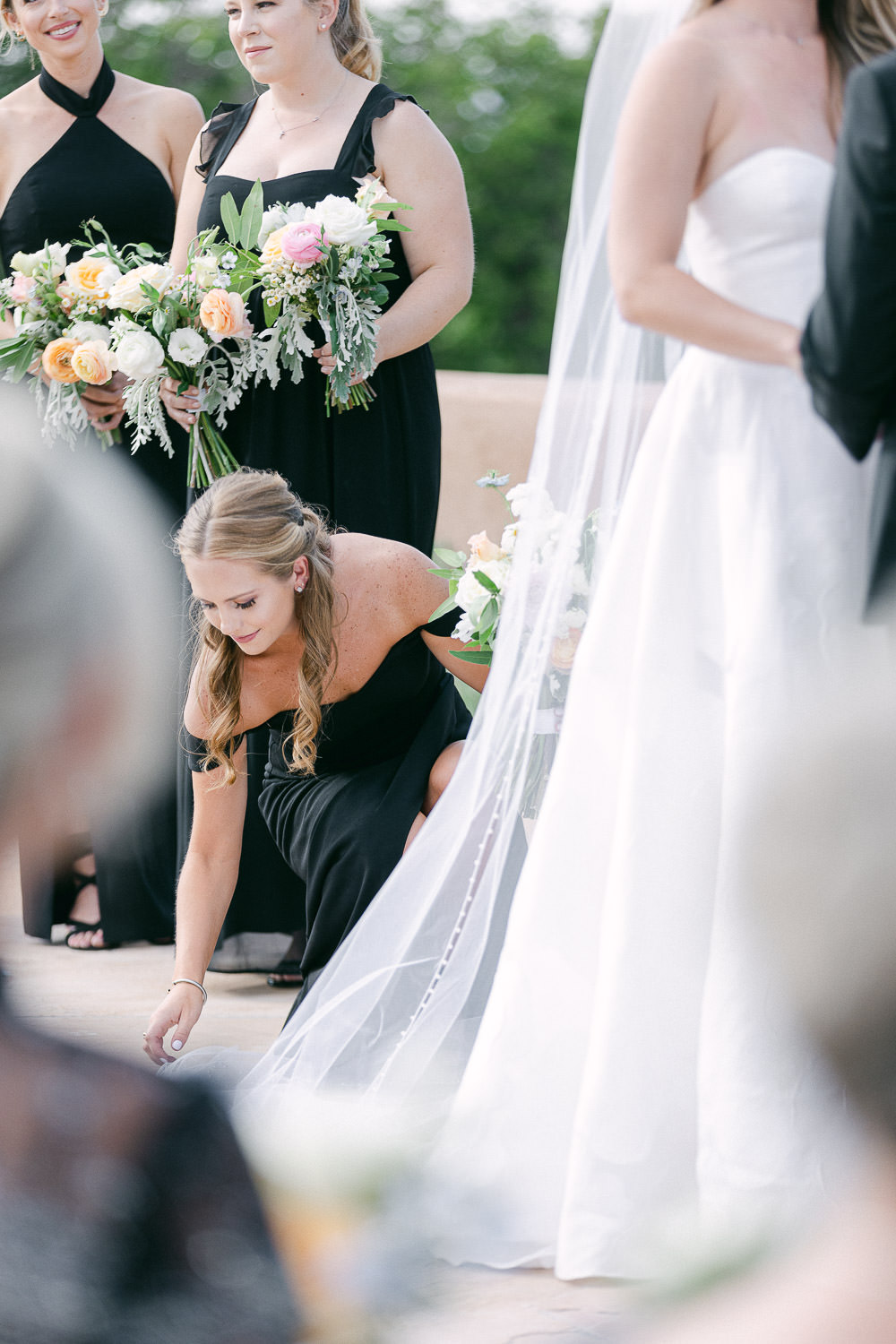 Maid of honor fixes bride's dress during wedding ceremony.